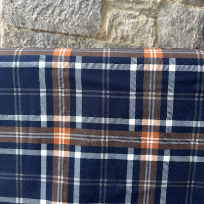 Plaid fabric with blue, brown, and white pattern against a stone wall background